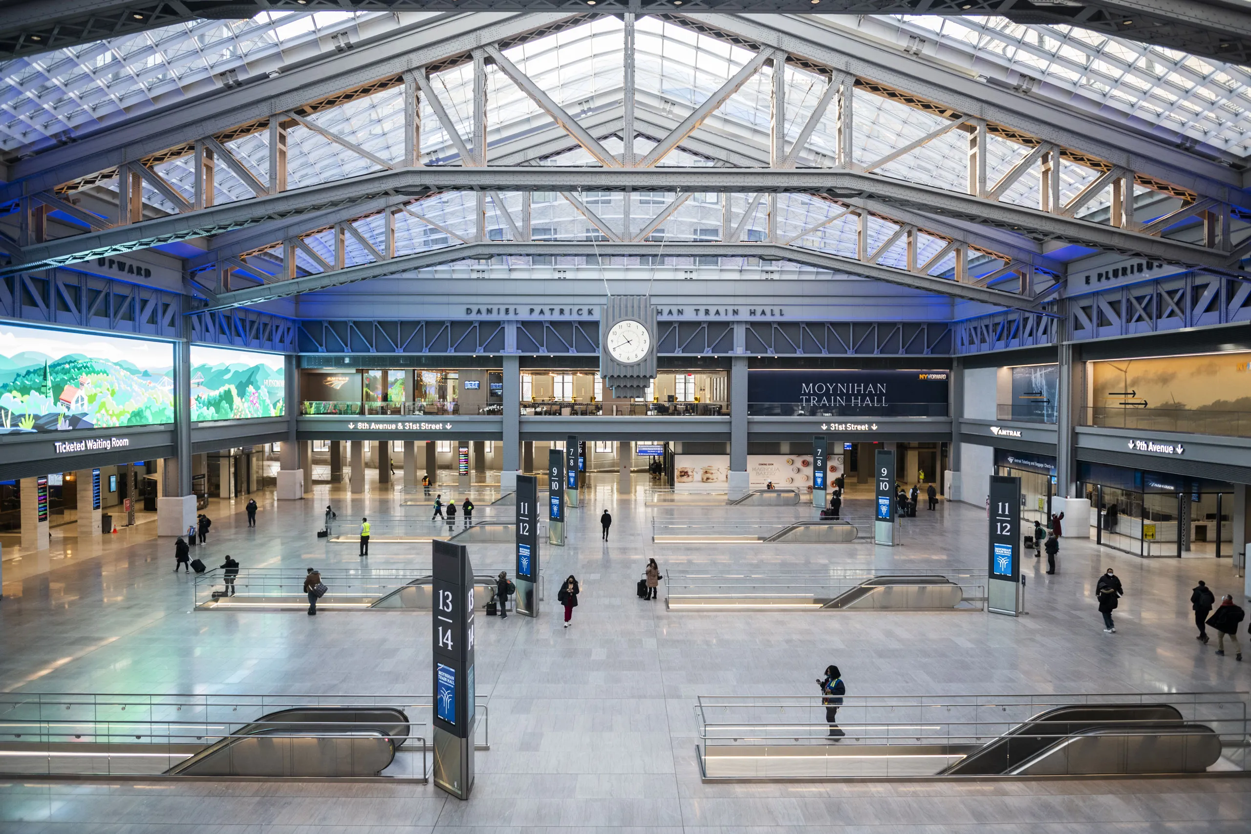 Long arrival hall at dusk with a polished stone floor, warm ceiling lights in a receding line, a traveller pulling a hard-shell suitcase toward distant glass doors, and a departure board glowing above a quiet ticket barrier, 1920x1080